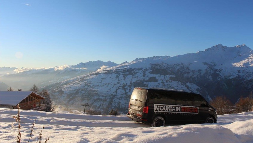 Minibus doing down snow covered road with mountains in background