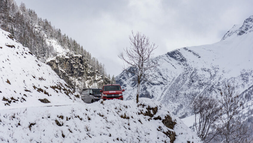 Two vans coming around the corner of a snow mountain pass