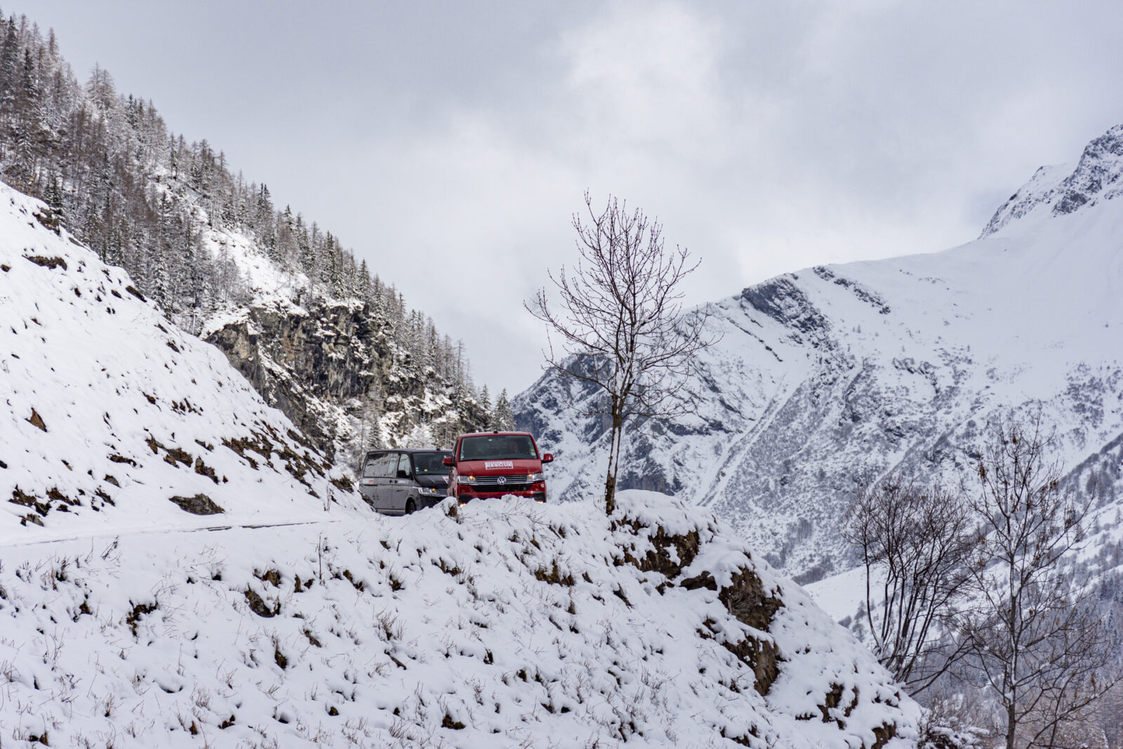 Two vans coming around the corner of a snow mountain pass
