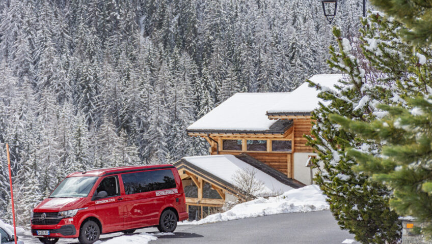 Red van parked outside ski chalets surrounded by snow covered trees