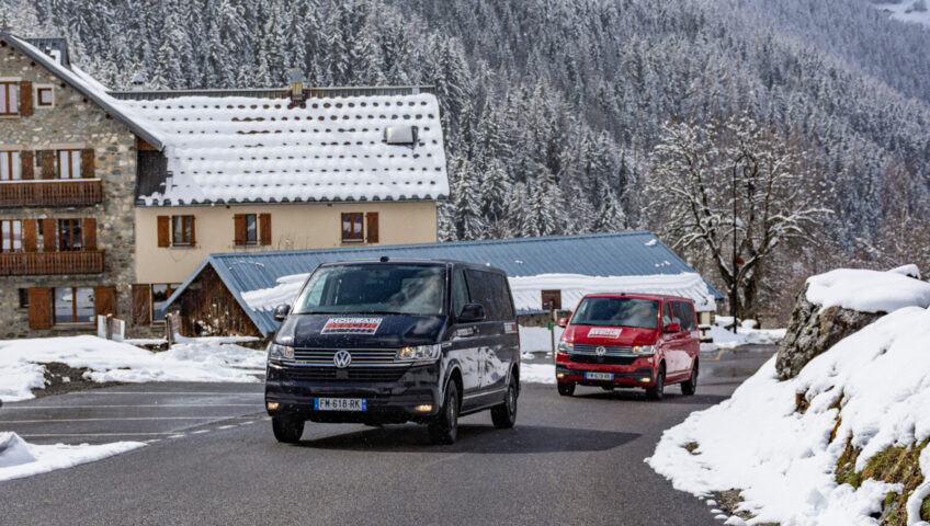 Black and red VW minibuses driving up road in a ski resort