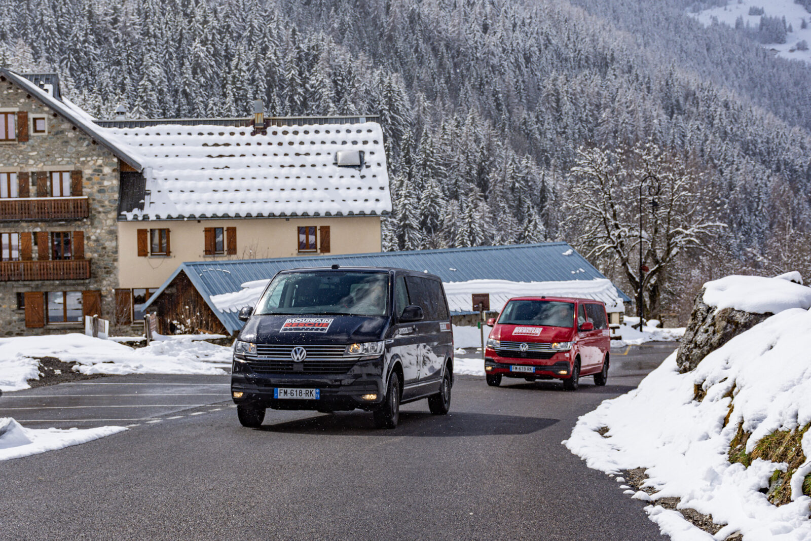 Black and red VW minibuses driving up road in a ski resort