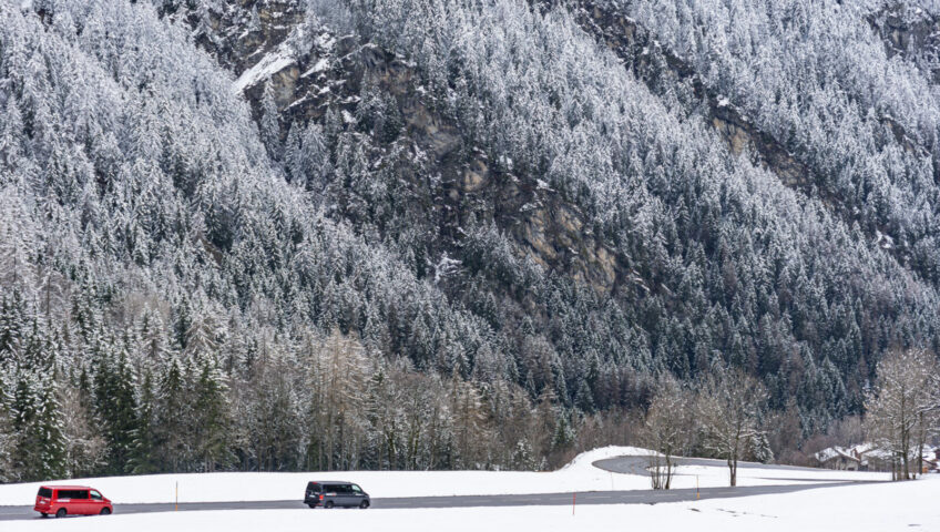 Mountain road with 2 Volkswagen 4motion vans driving surrounded by snow covered trees.
