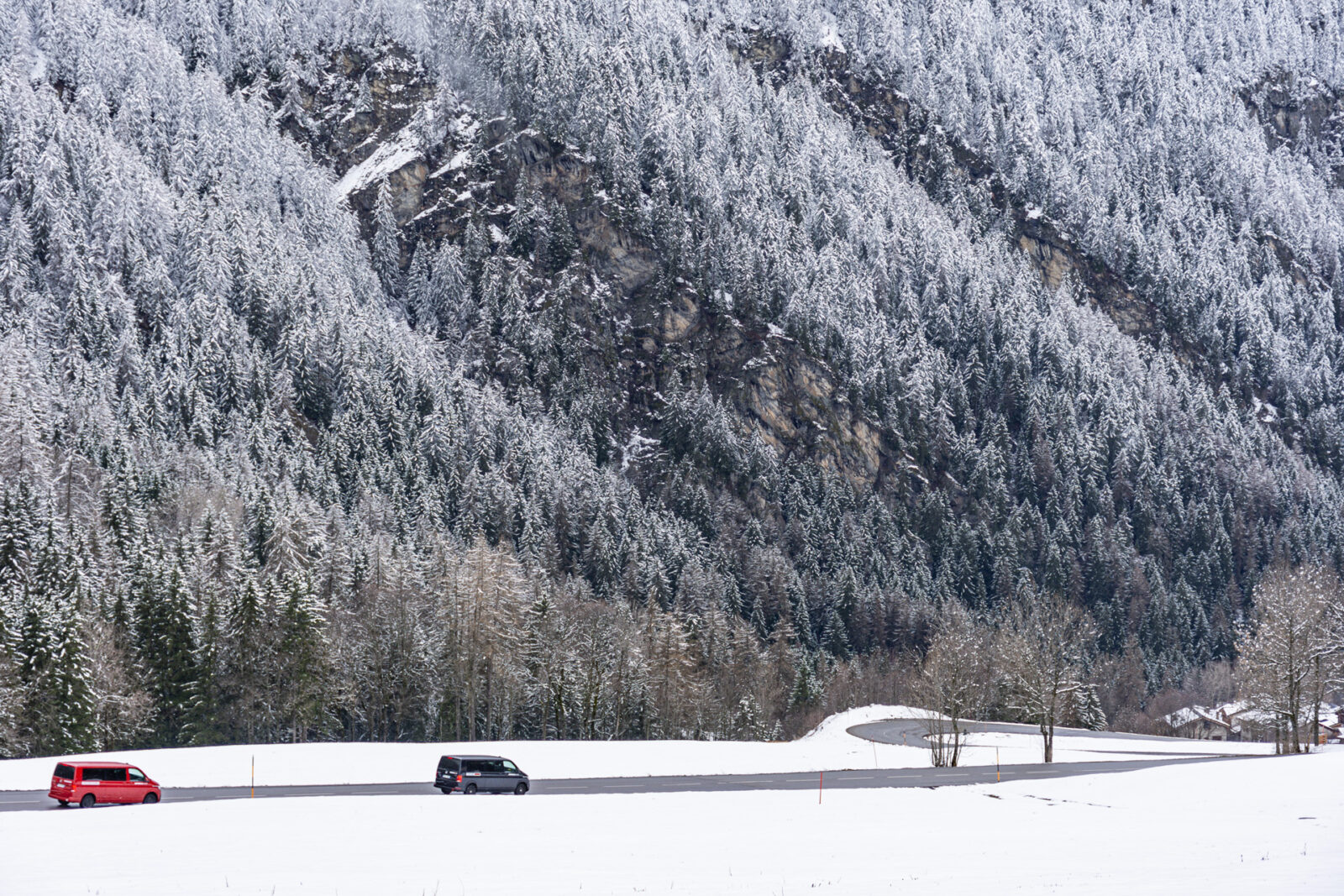 Mountain road with 2 Volkswagen 4motion vans driving surrounded by snow covered trees.