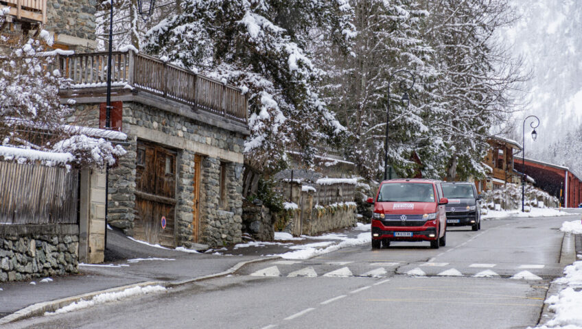 Two VW Vans driving down mountain village road in the winter